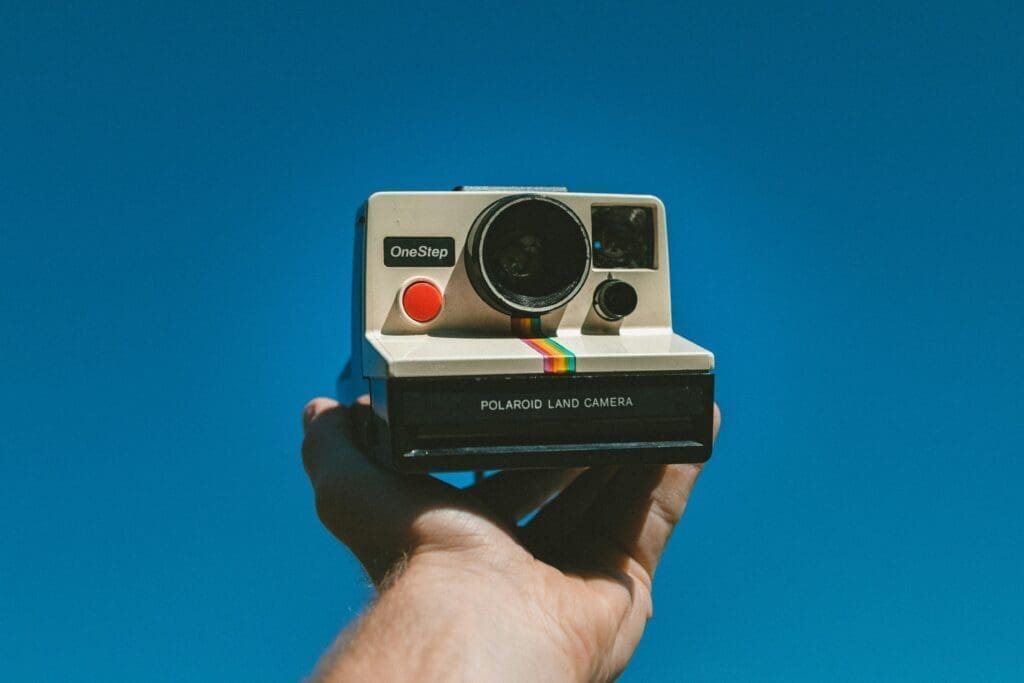 Polaroid Hand holding a vintage Polaroid OneStep Land Camera against a clear blue sky