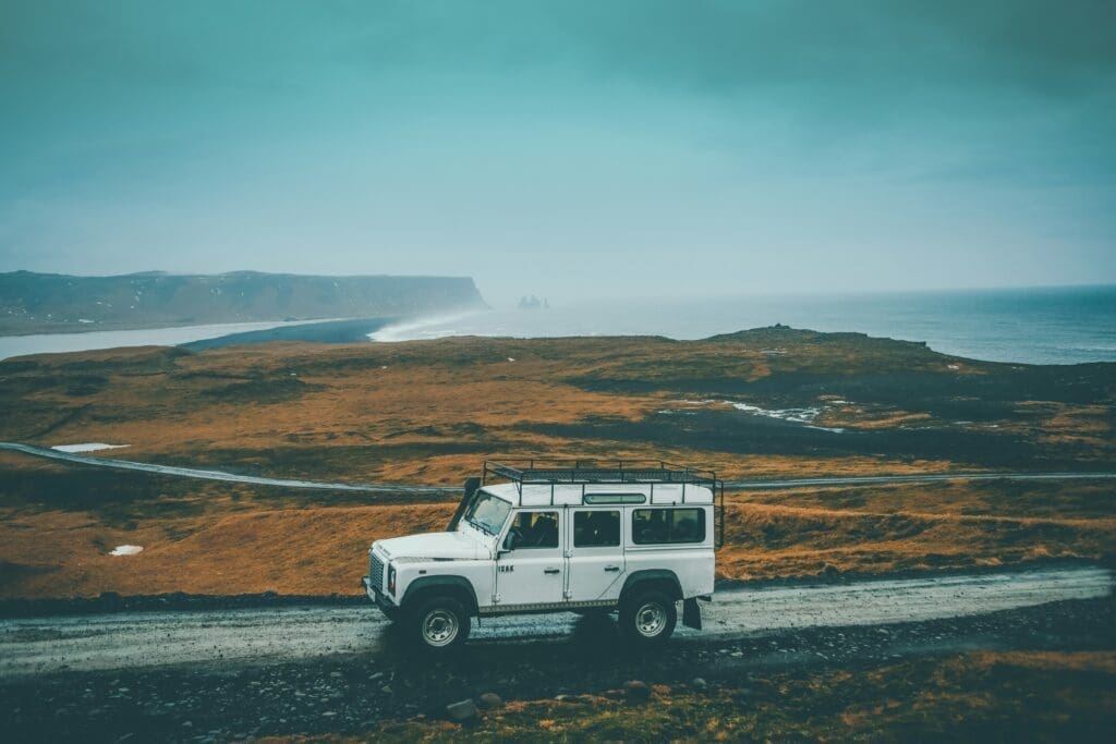Land Rover White Land Rover driving along a rugged coastal road with dramatic cliffs and ocean in the background on a cloudy day