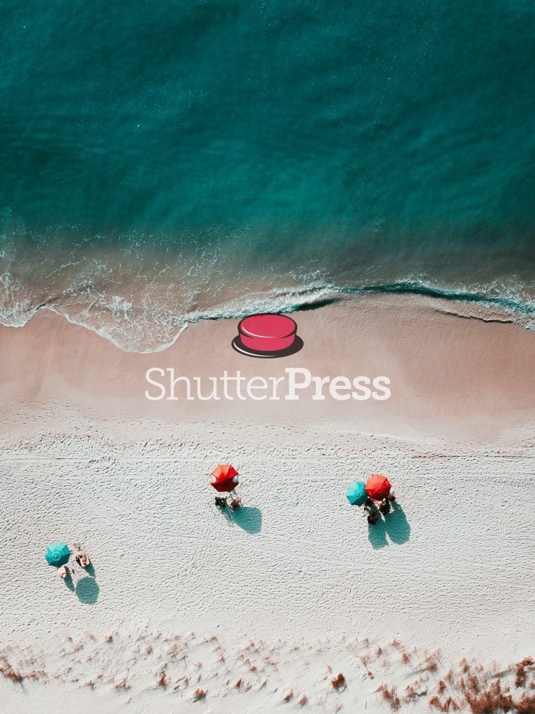Aerial view of turquoise sea and sandy beach with red umbrellas and ShutterPress logo watermark