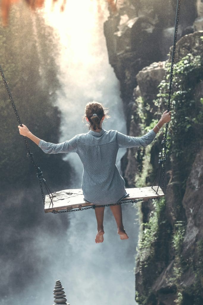Woman on a wooden swing overlooking a dramatic waterfall and rocky canyon, travel adventure scene