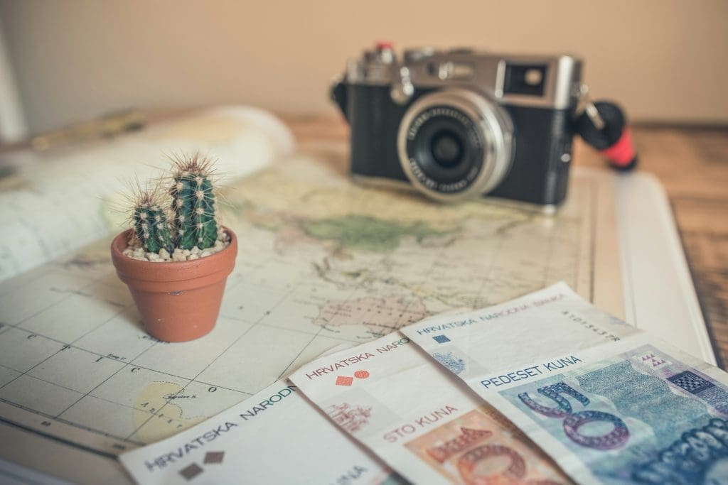 Photo by chris lawton on unsplash Close up of travel essentials with Croatian kuna banknotes, a small cactus in a terracotta pot, a vintage camera, and a world map