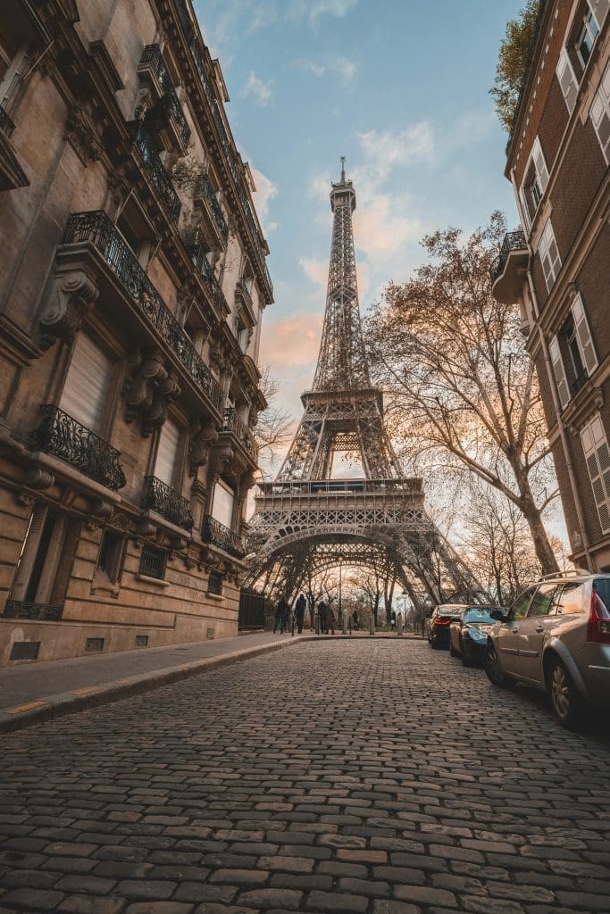Photo by cyril on unsplash View of the Eiffel Tower from a cobblestone street in Paris, framed by classic Parisian buildings at sunset