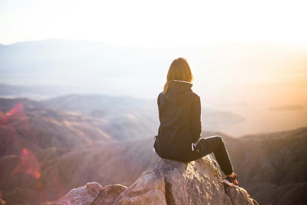 Photo by denys nevozhai on unsplash Woman sitting on a rock overlooking a mountain landscape at sunrise