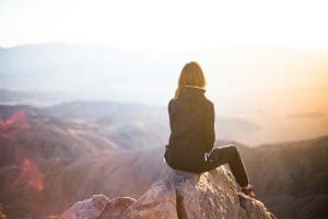 Woman sitting on a rock overlooking a mountain landscape at sunrise