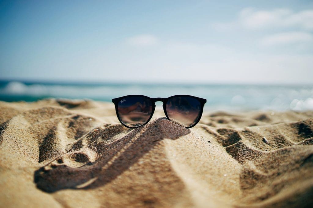 Photo by ethan robertson on unsplash Black sunglasses resting on a sandy beach with the sea and sky in the background
