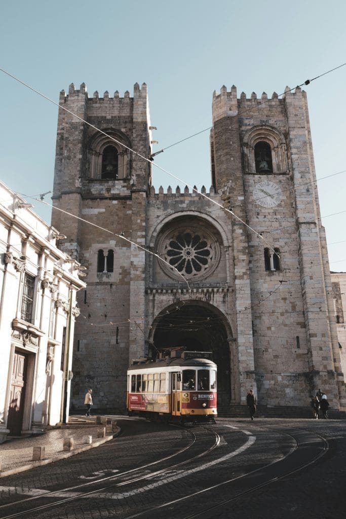 Historic yellow Lisbon tram passing in front of the Lisbon Cathedral (Sé de Lisboa) on a sunny day in Portugal