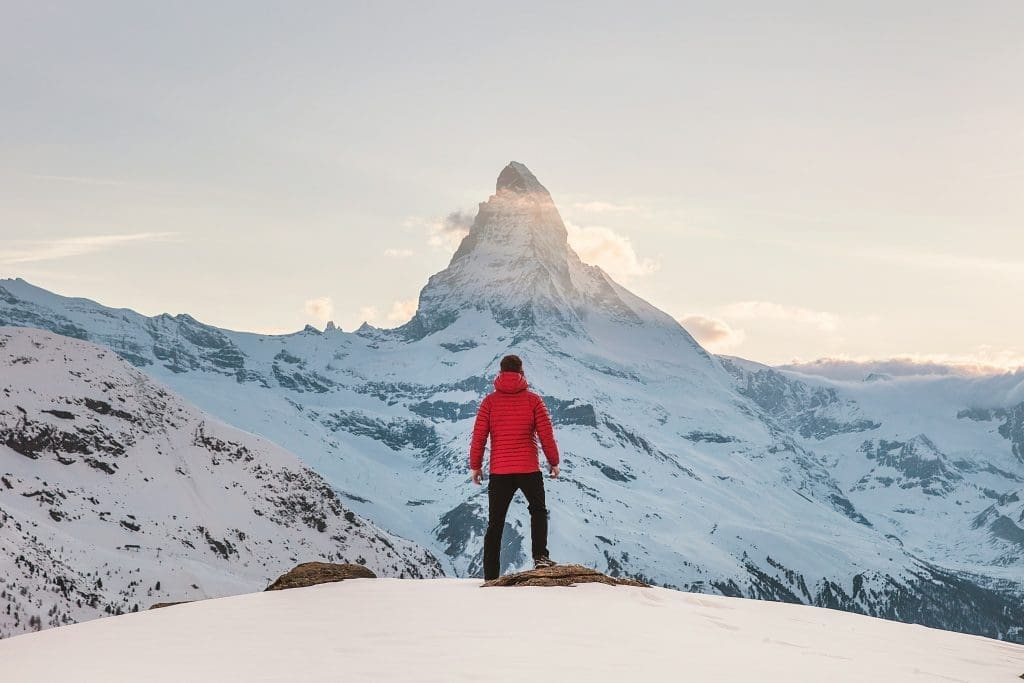 Photo by joshua earle on unsplash Man in red jacket standing on snowy mountain overlooking the Matterhorn at sunrise in Switzerland