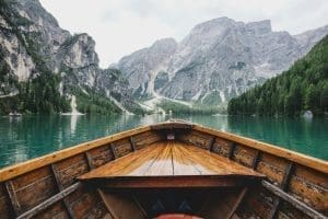 Wooden boat on turquoise lake surrounded by pine forests and dramatic mountains in the Italian Dolomites