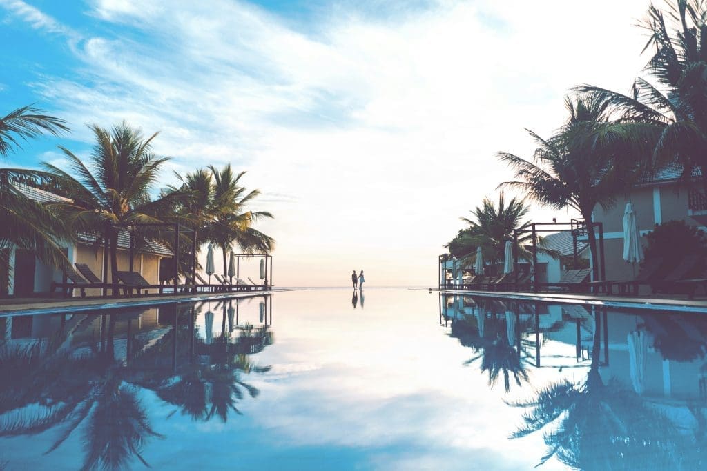 Photo by marvin meyer on unsplash Couple walking by an infinity pool at a tropical resort with palm trees and reflections at sunset