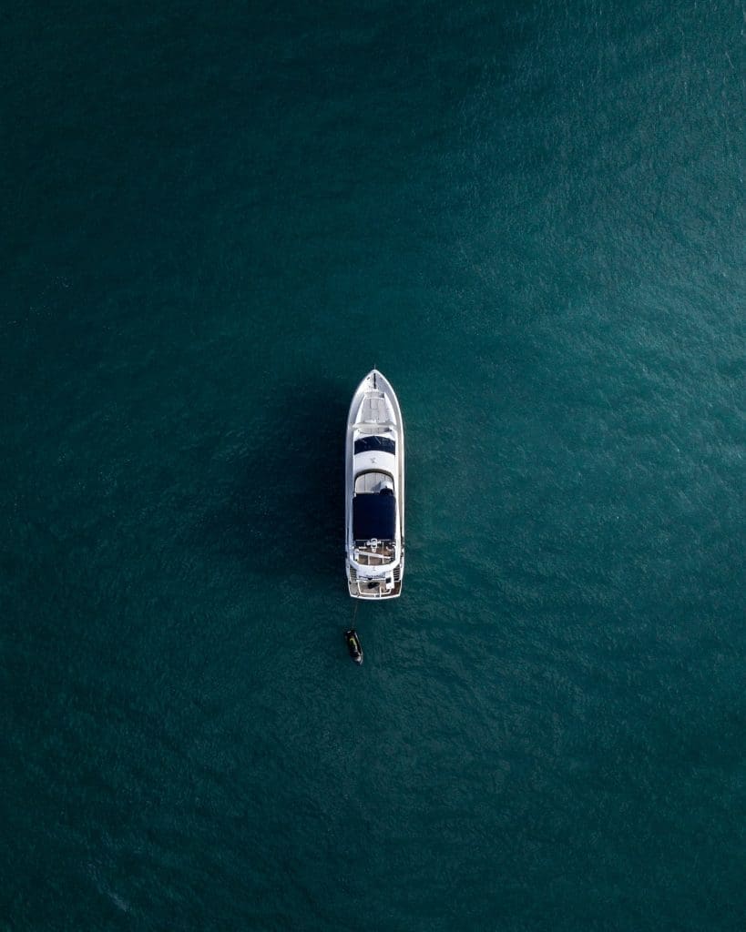 Aerial view of a yacht anchored in calm blue water with a small dinghy nearby