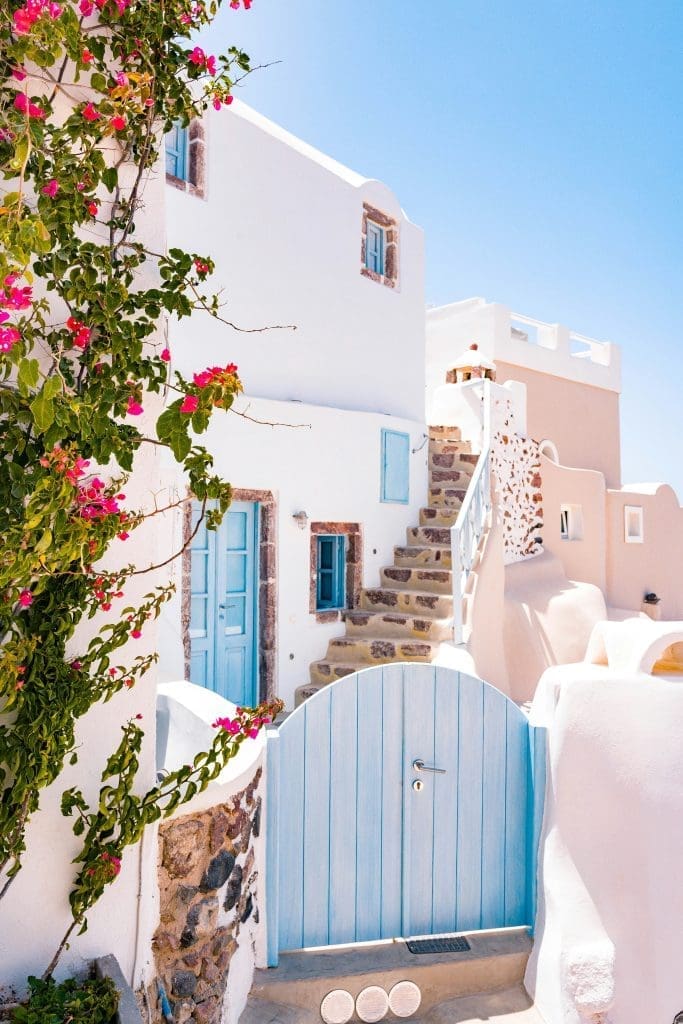 Traditional whitewashed houses with blue doors and windows in Santorini, Greece, with pink bougainvillaea flowers
