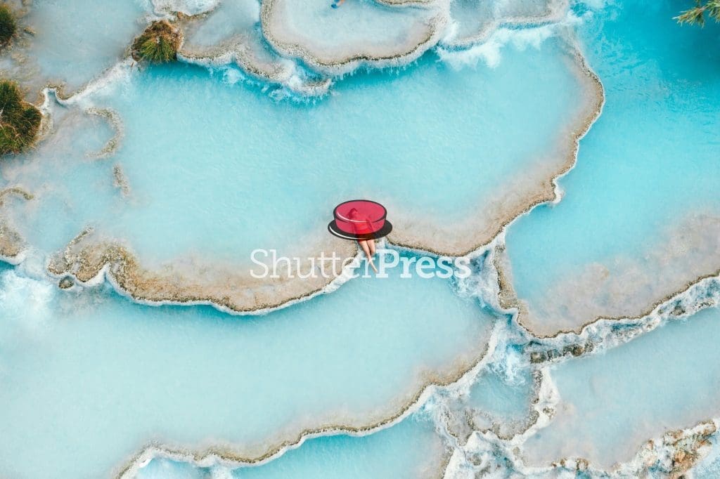Aerial view of natural turquoise thermal pools with stone edges, person relaxing in water, ShutterPress watermark