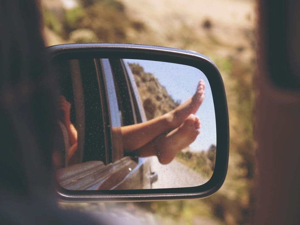 Photo by Anja on Unsplash Car wing mirror reflection showing bare feet hanging out of window on sunny road trip