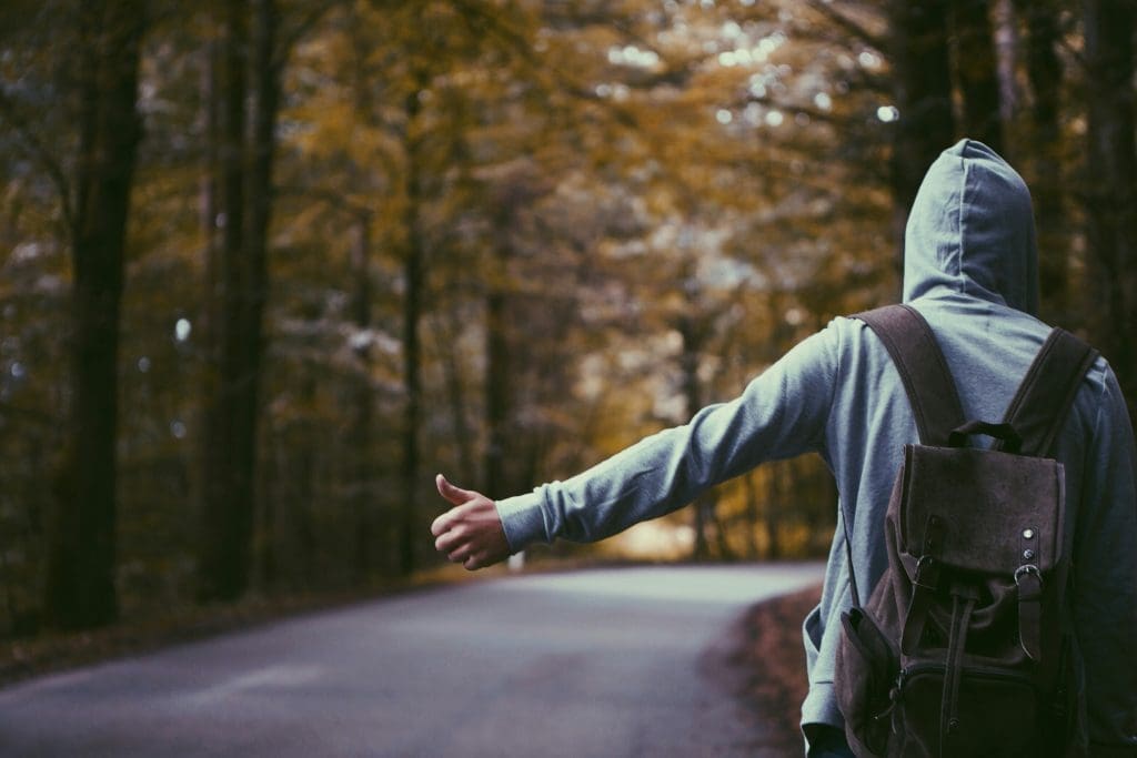 Photo by Atlas Green on Unsplash Traveller in grey hoodie with backpack hitchhiking on empty forest road in autumn