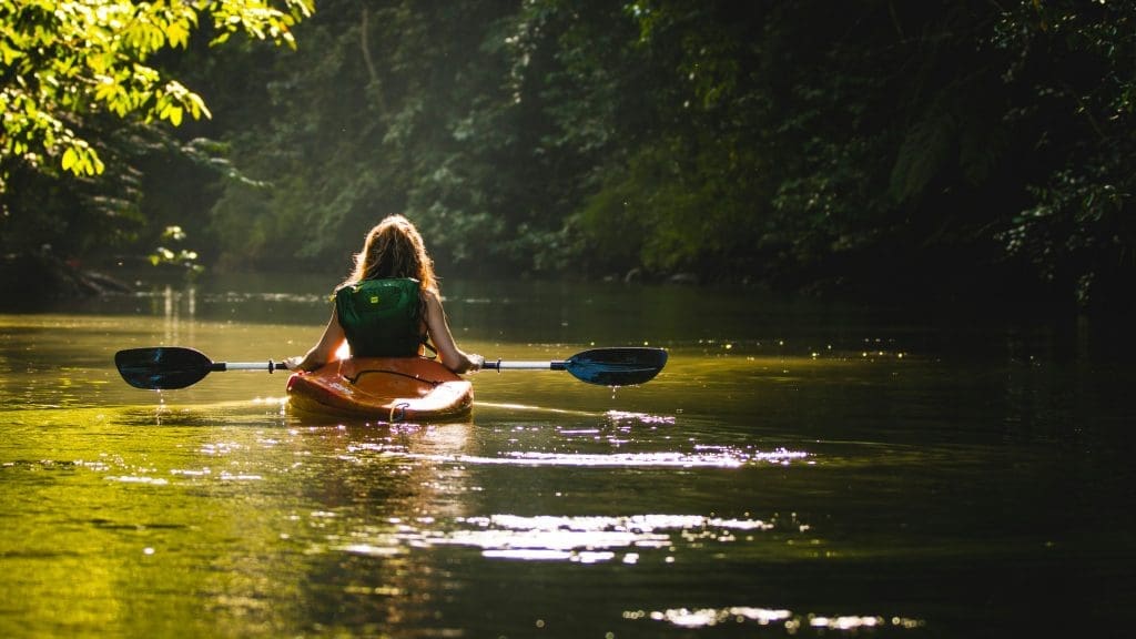 Photo by Filip Mroz on Unsplash Woman kayaking on calm river surrounded by lush green forest with sunlight on water