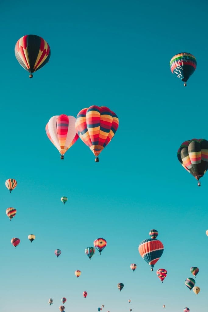 Photo by Ian Dooley on Unsplash A cluster of brightly coloured hot air balloons drifting against a clear turquoise sky.