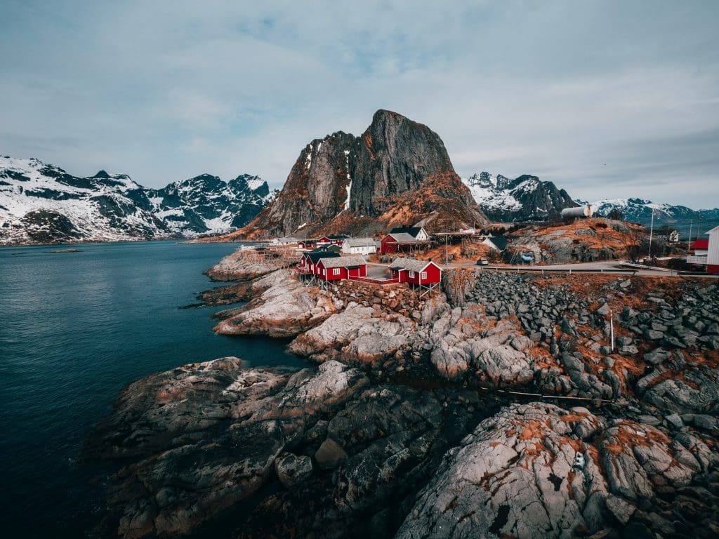 Photo by John O Nolan on Unsplash Red fishing cabins on rocky shore with snow-capped mountains and fjord in Lofoten Norway