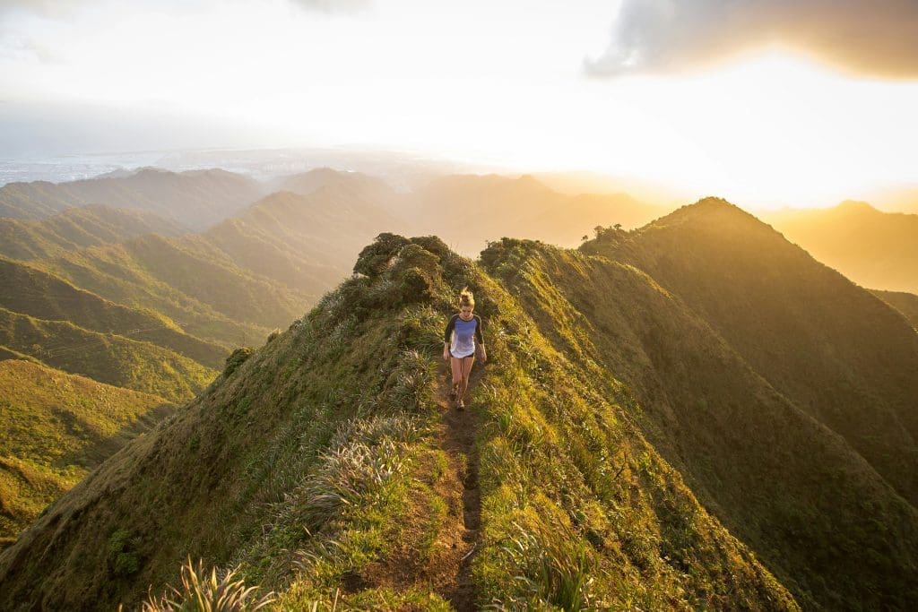 Photo by Kalen Emsley on Unsplash Woman hiking along narrow mountain ridge at sunset with golden light over green valleys