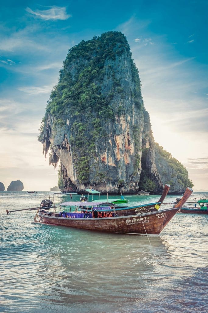 Photo by Marcin Kalinski on Unsplash Traditional longtail boat floating on turquoise sea with towering limestone cliff in Krabi Thailand