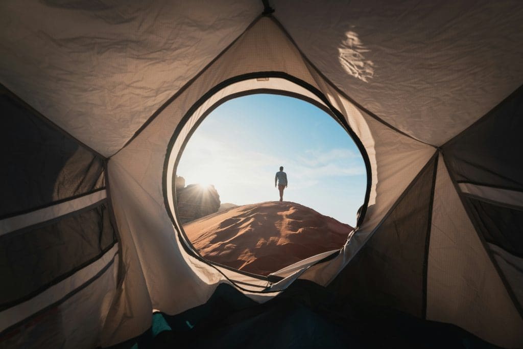Photo by Neom on Unsplash View from inside tent looking out at man standing on desert dune under bright morning sky