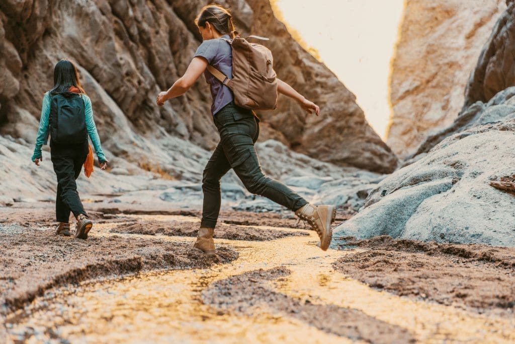 Photo by Neom on Unsplash Two women hiking through narrow desert canyon crossing shallow stream in golden light