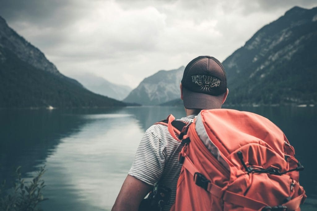 Photo by Philipp Kammerer on Unsplash Hiker in red rucksack gazing at mountain lake and range in alpine landscape