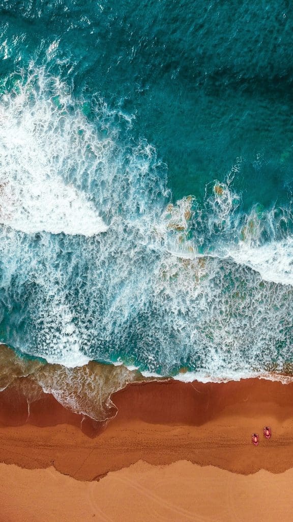 Photo by Will Turner on Unsplash Aerial view of turquoise waves crashing on golden sandy beach with two red kayaks on shore